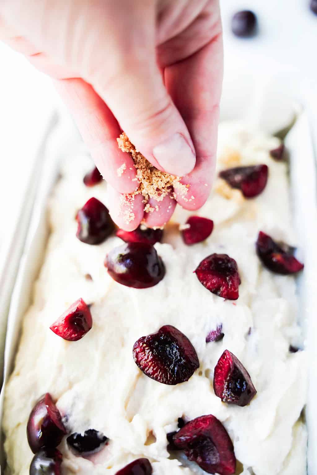 Cherry bread batter topped with cherry halves and brown sugar before baking.