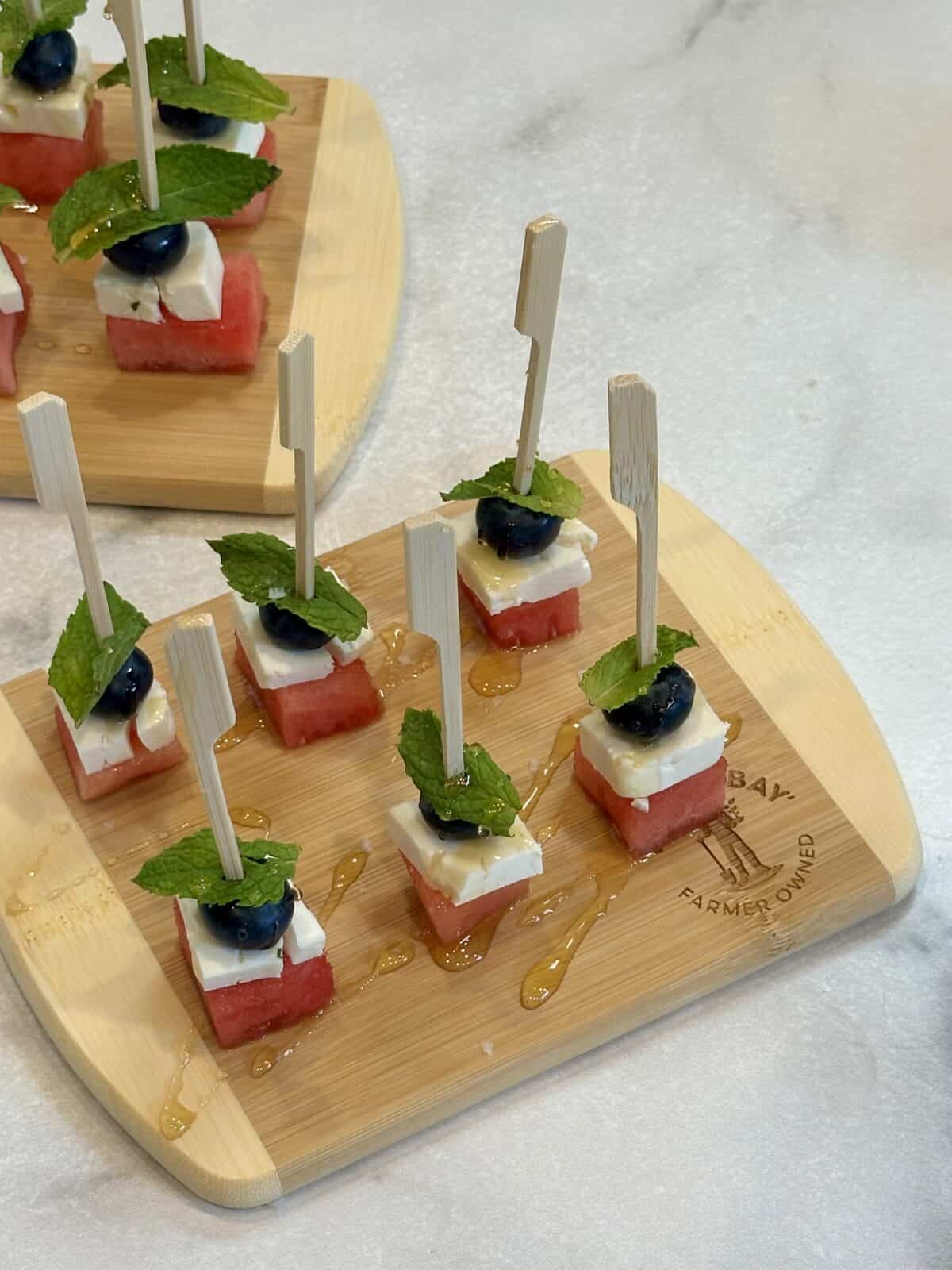 vertical image of watermelon, feta, blueberry and mint leaf drizzled with honey on cutting board