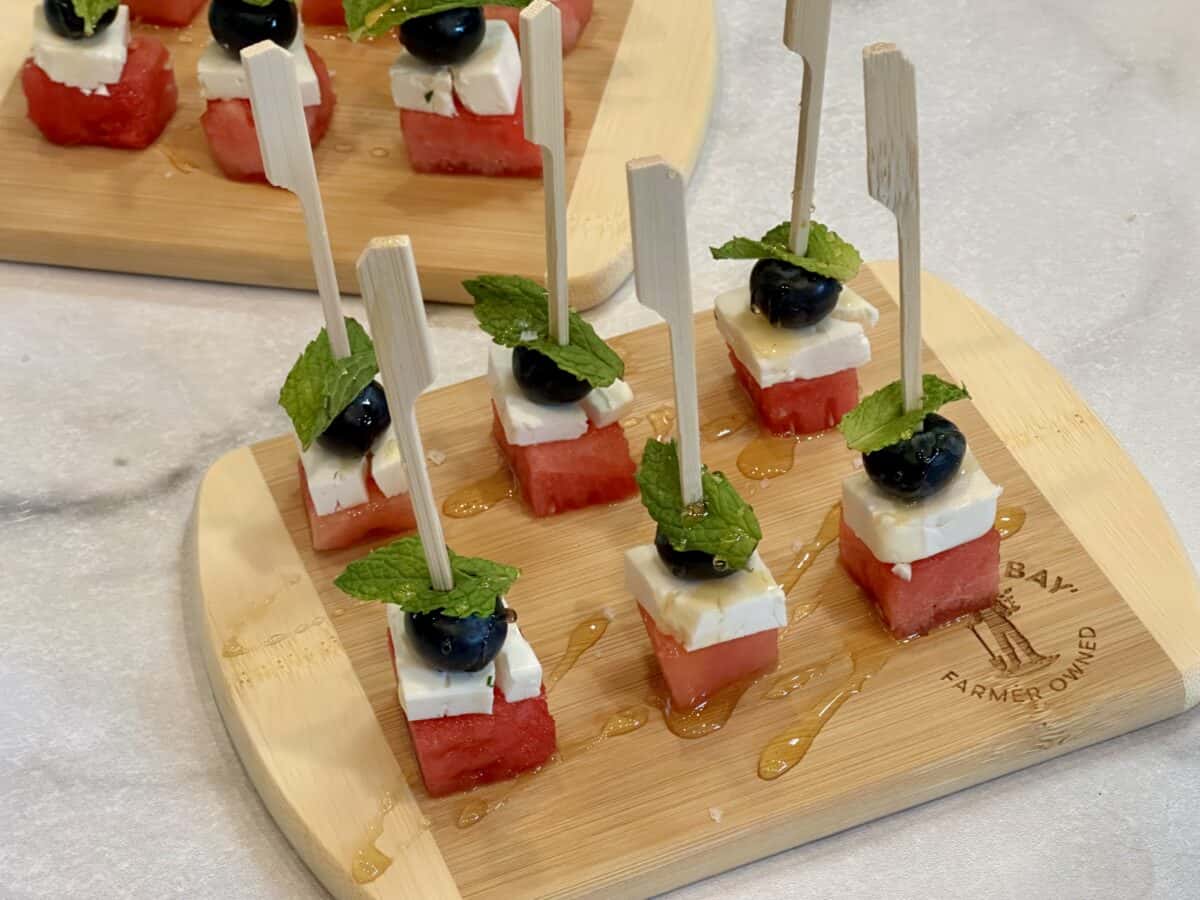 horitzontal image of 6 watermelon and feta skewers on cutting board drizzled with honey