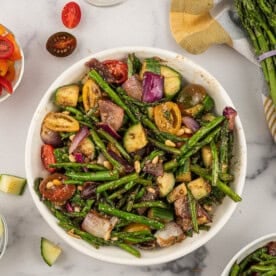 Grilled asparagus salad with fresh tomatoes, cucumbers, and asparagus around the bowl.