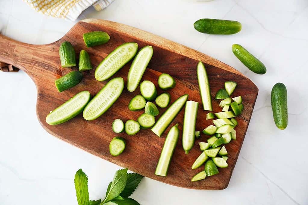 Different styles and cuts of baby cucumbers on a wood cutting board