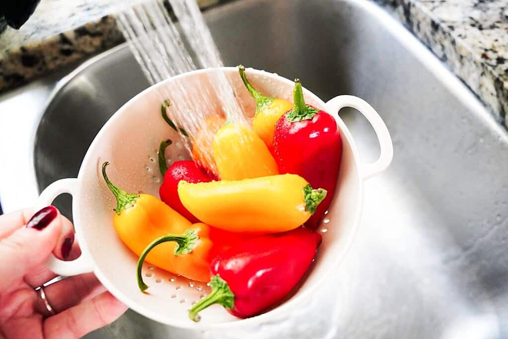 Washing sweet mini peppers in a collander over a sink