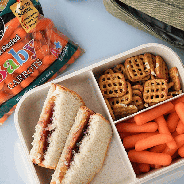 Baby carrots in a bento box with PBJ & pretzels with a Grimmway Farms bag of baby carrots