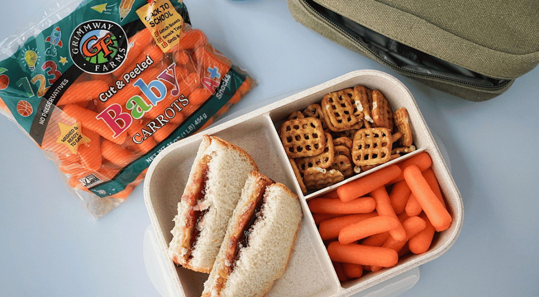 Baby carrots in a bento box with PBJ & pretzels with a Grimmway Farms bag of baby carrots