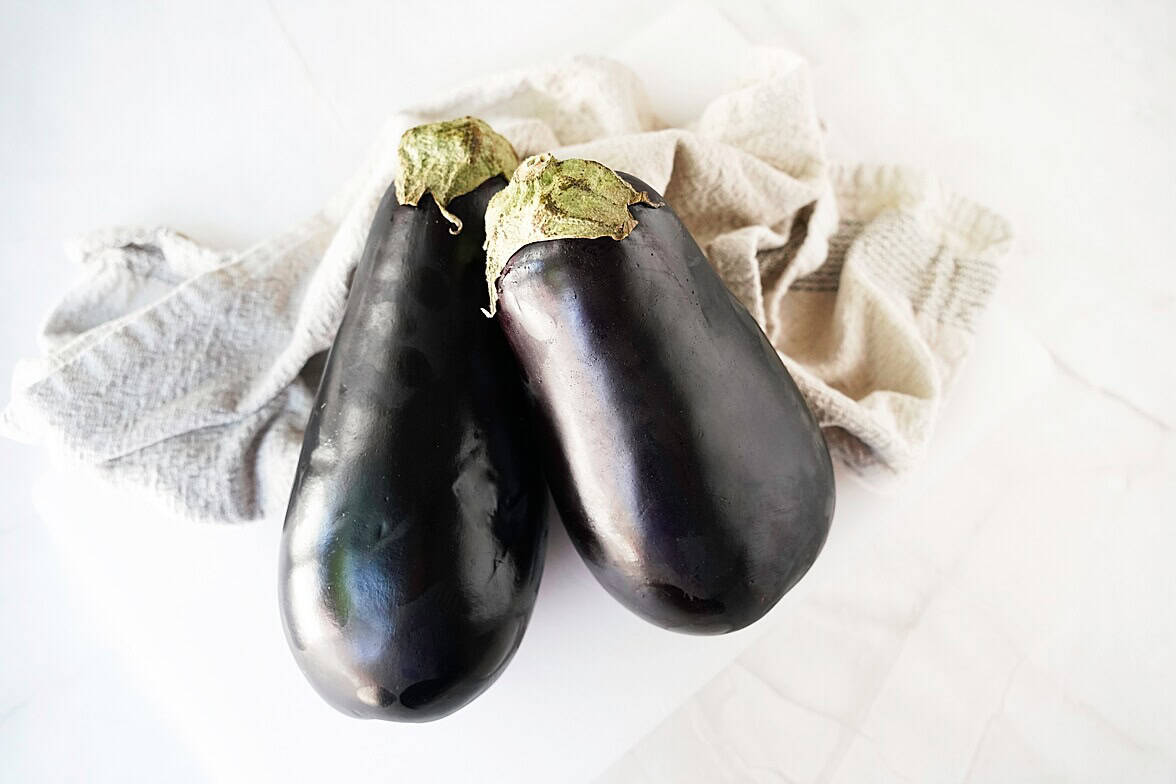Two whole eggplants on white counter on top of a towel