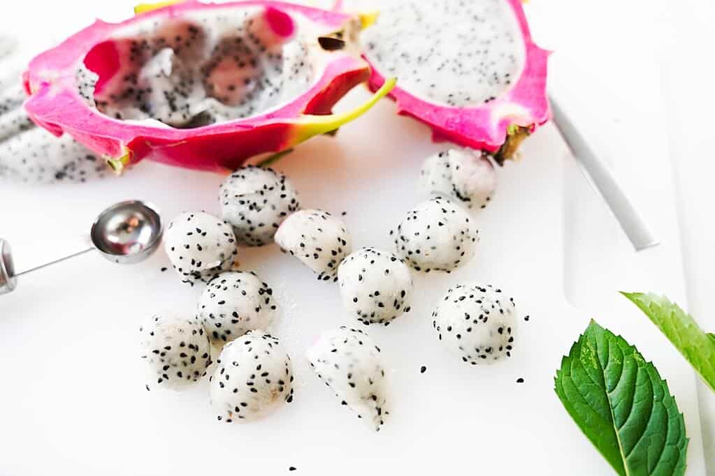 Dragon fruit balls next to a melon baller and cut open dragon fruit