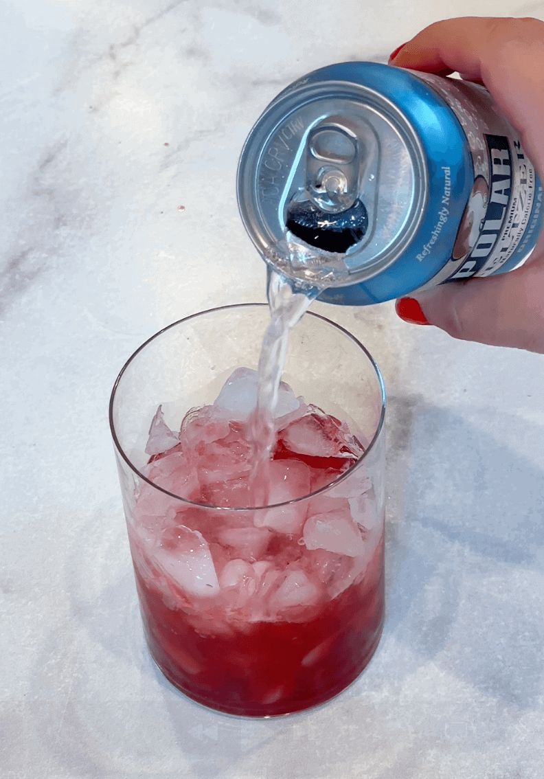 pouring soda into glass with raspberry simple syrup and ice