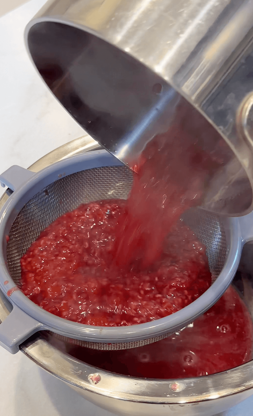 straining boiling raspberry mixture into raspberry simple syrup.