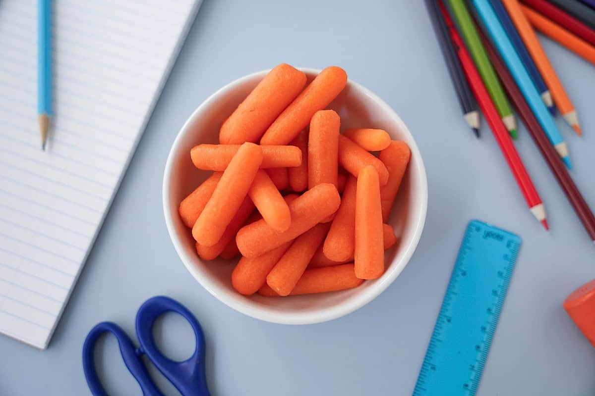 baby carrots in a ramekin on a table with school supplies