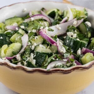 Smashed cucumber salad in a bowl with feta and onions