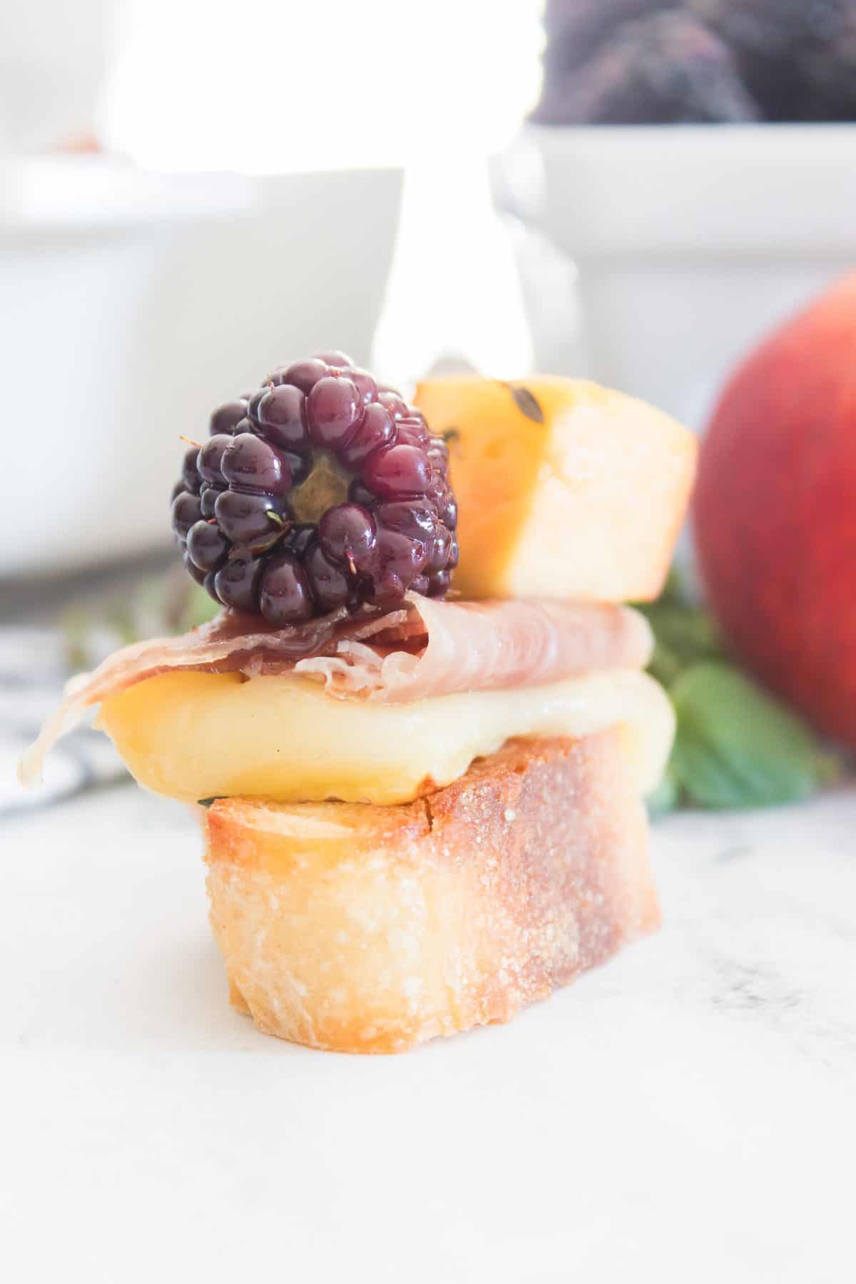 Toasted baguette topped with melted brie, prosciutto, fresh blackberry, and peach for an easy sweet and savory appetizer.