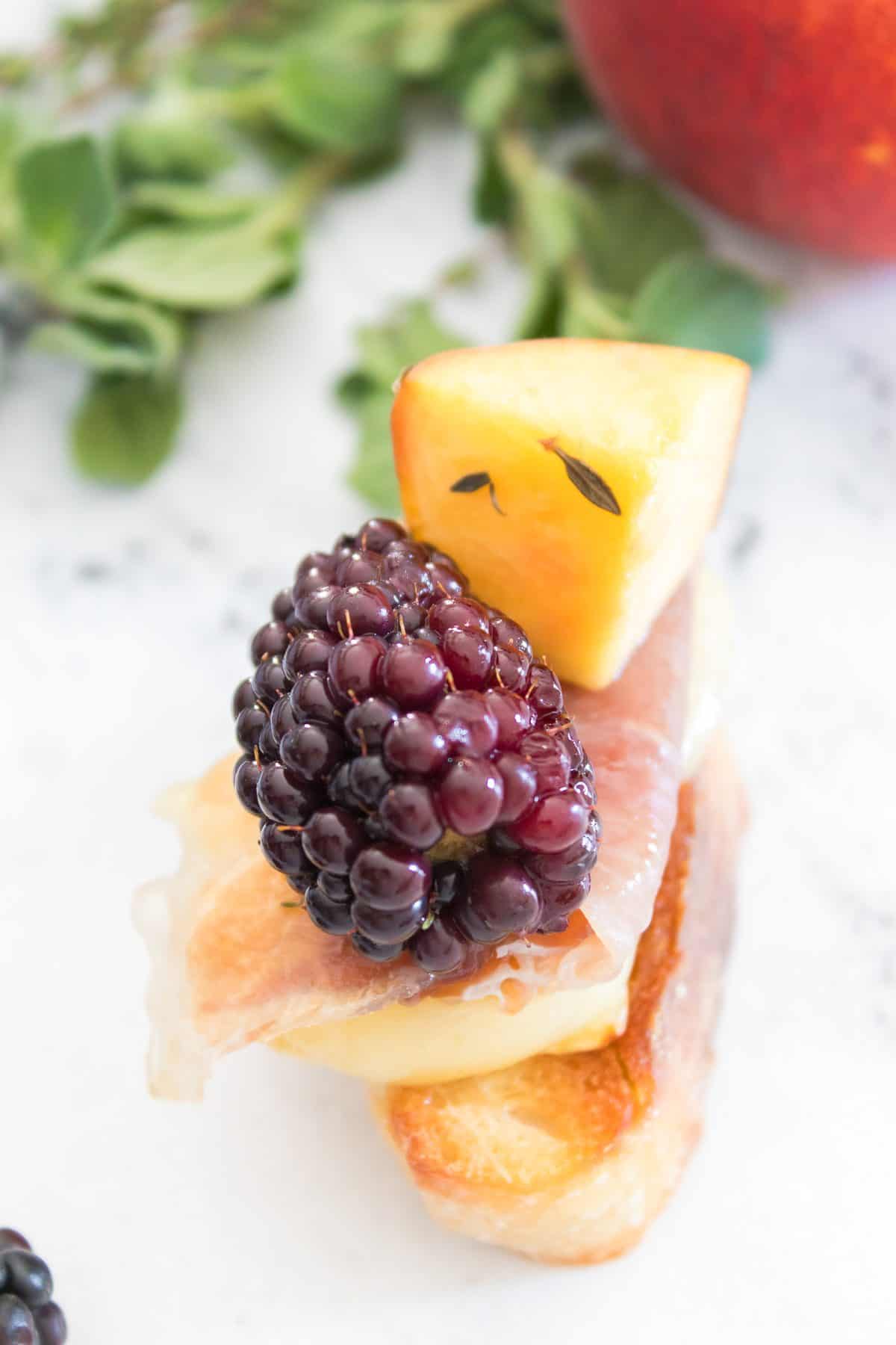 Toasted baguette topped with melted brie, prosciutto, fresh blackberry, peach, herbs, and a drizzle of hot honey.