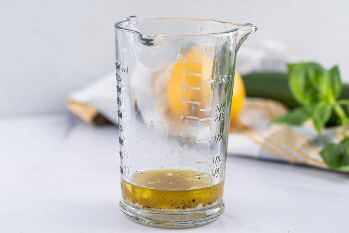 Olive oil, lemon juice, garlic, salt, pepper, and red pepper flakes mixed in a measuring glass.
