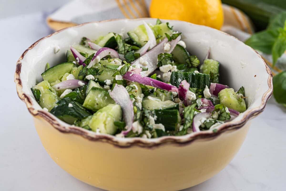 Smashed cucumber salad in a large serving bowl with crumbled feta, torn basil, and sliced red onions.