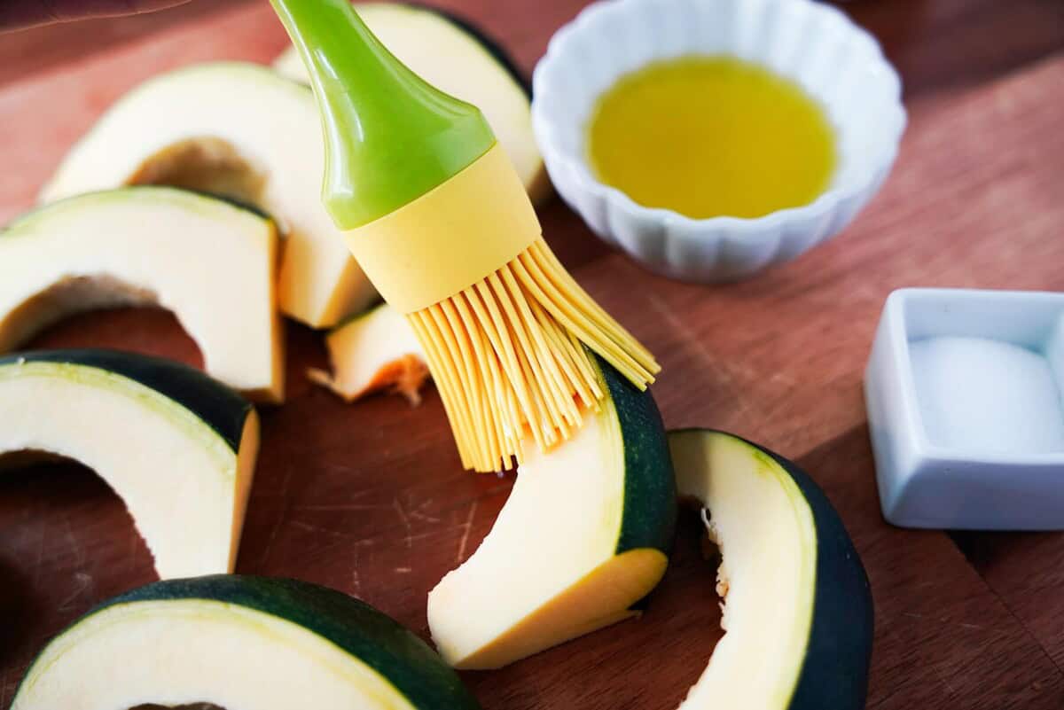 Adding olive oil to acorn squash pieces with a basting brush